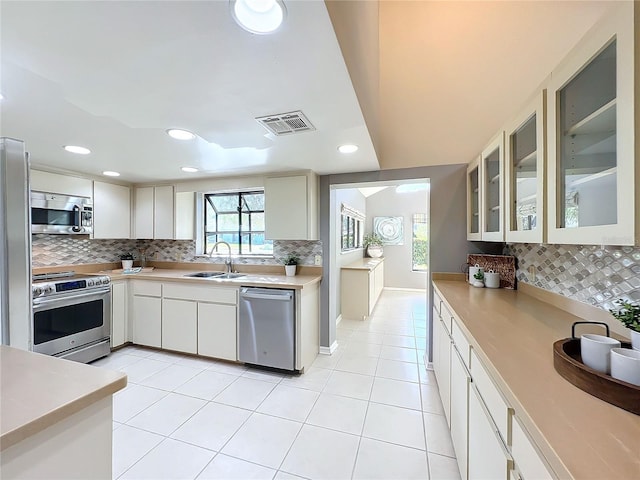 kitchen featuring sink, backsplash, white cabinetry, stainless steel appliances, and light tile patterned floors