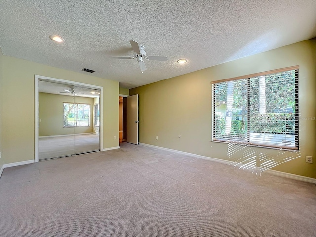 unfurnished bedroom with a closet, a textured ceiling, light colored carpet, and ceiling fan