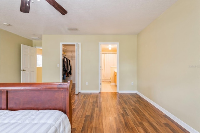 unfurnished bedroom featuring a walk in closet, ensuite bath, dark hardwood / wood-style flooring, a closet, and ceiling fan