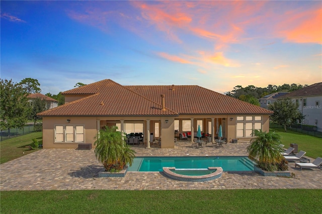 back house at dusk with a lawn, a patio, and a pool with hot tub