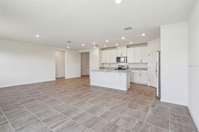 kitchen featuring white cabinetry, light stone countertops, a kitchen breakfast bar, a center island with sink, and appliances with stainless steel finishes