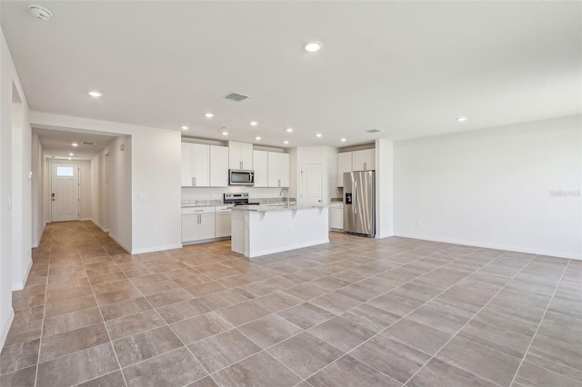 kitchen featuring sink, light stone counters, a kitchen island with sink, white cabinets, and appliances with stainless steel finishes