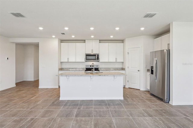 kitchen with white cabinetry, light stone counters, an island with sink, and stainless steel appliances