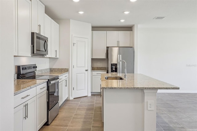 kitchen featuring white cabinetry, sink, light stone countertops, stainless steel appliances, and a kitchen island with sink