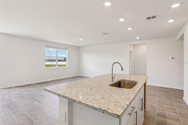 kitchen featuring white cabinets, light stone countertops, sink, and an island with sink