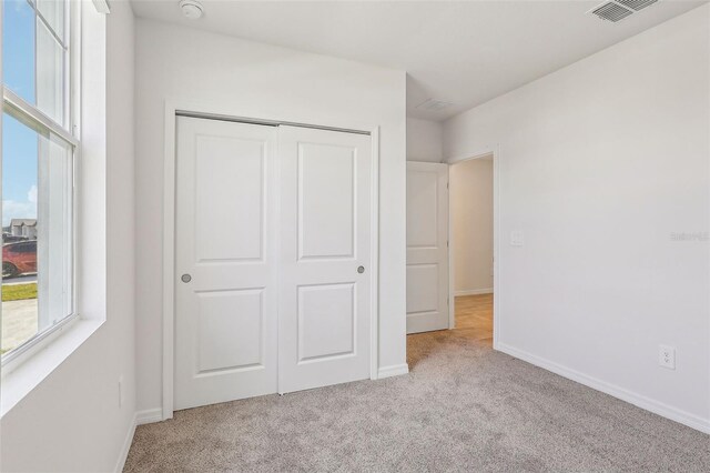 unfurnished bedroom with light colored carpet and a closet