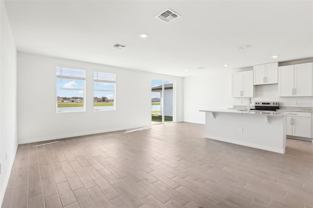 kitchen with stainless steel range with electric stovetop, a breakfast bar, sink, a center island with sink, and white cabinetry