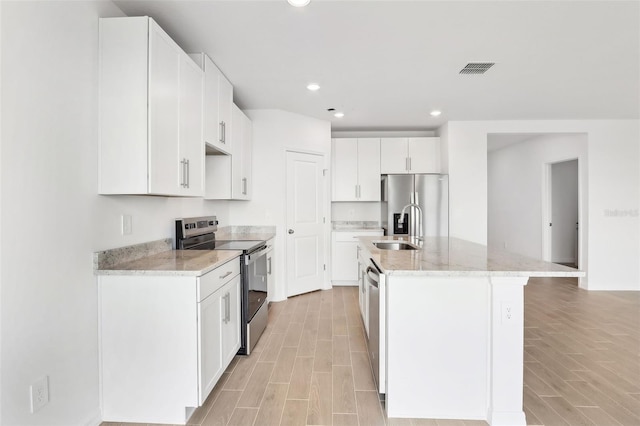 kitchen featuring light stone counters, stainless steel appliances, sink, a center island with sink, and white cabinetry