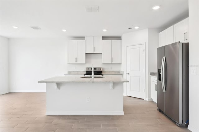 kitchen featuring a kitchen breakfast bar, white cabinetry, a center island with sink, and stainless steel appliances