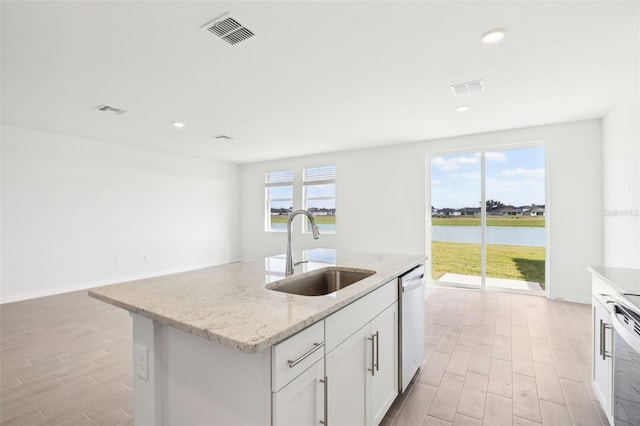 kitchen featuring dishwasher, white cabinets, a water view, sink, and an island with sink