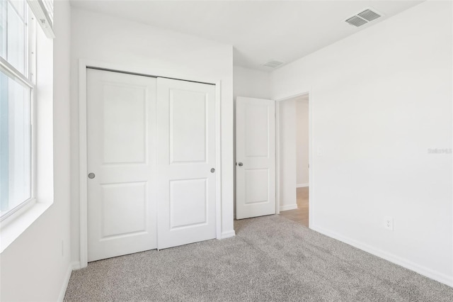 unfurnished bedroom with multiple windows, light carpet, and a closet