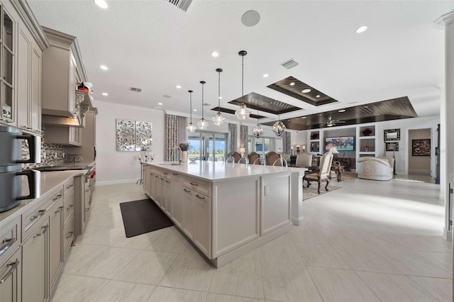 kitchen featuring hanging light fixtures, light tile patterned floors, a large island with sink, gray cabinetry, and crown molding