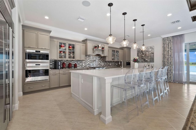 kitchen featuring a large island with sink, double oven, a breakfast bar area, ornamental molding, and decorative light fixtures