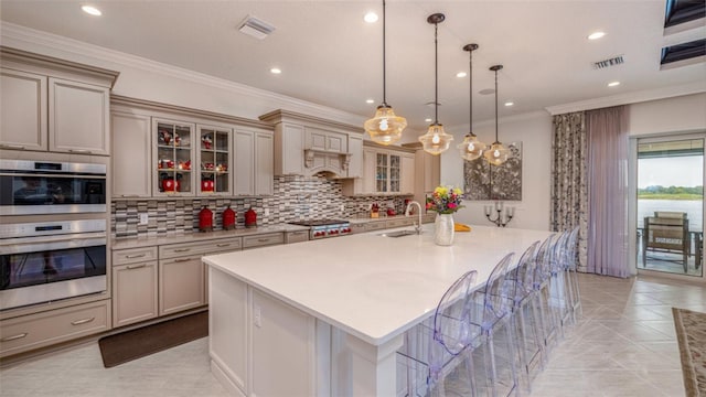 kitchen featuring light tile patterned floors, hanging light fixtures, appliances with stainless steel finishes, and a kitchen island with sink