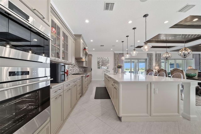 kitchen featuring a large island with sink, stainless steel double oven, hanging light fixtures, crown molding, and a kitchen bar