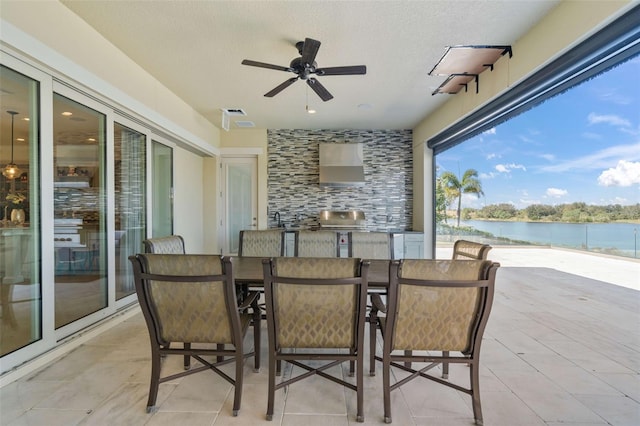 view of patio with an outdoor kitchen, grilling area, a water view, and ceiling fan