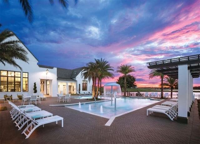 pool at dusk featuring pool water feature, a patio, and a pergola