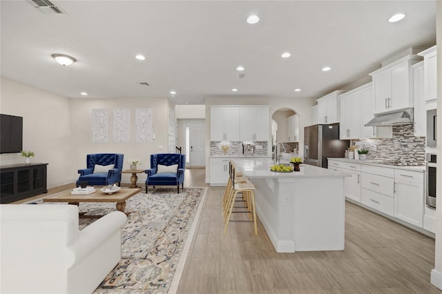 kitchen featuring appliances with stainless steel finishes, a kitchen breakfast bar, white cabinetry, light hardwood / wood-style floors, and a center island with sink