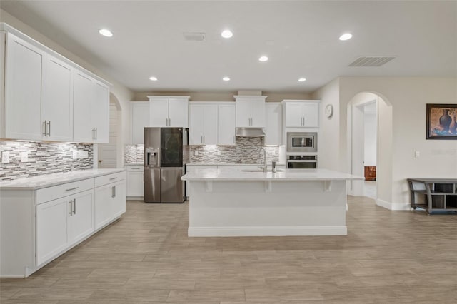 kitchen featuring a kitchen island with sink, tasteful backsplash, appliances with stainless steel finishes, and white cabinets