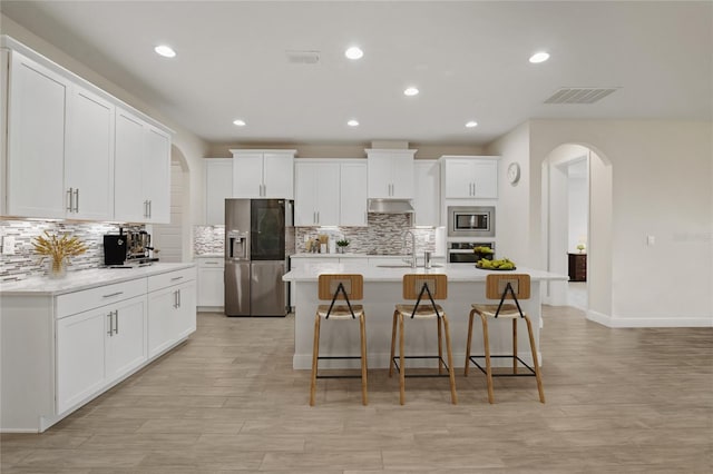 kitchen featuring a kitchen island with sink, appliances with stainless steel finishes, a breakfast bar, and white cabinets