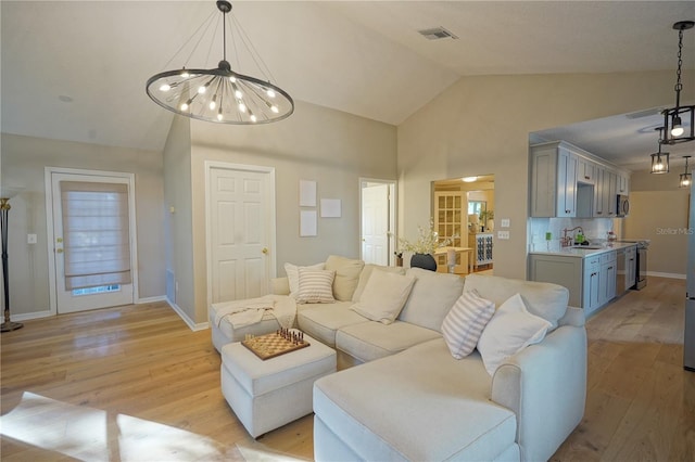 living room with an inviting chandelier, high vaulted ceiling, sink, and light hardwood / wood-style floors