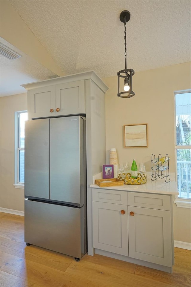 kitchen with stainless steel refrigerator, decorative light fixtures, light hardwood / wood-style floors, and a textured ceiling