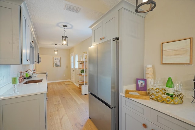 kitchen featuring sink, a textured ceiling, hanging light fixtures, light wood-type flooring, and stainless steel fridge