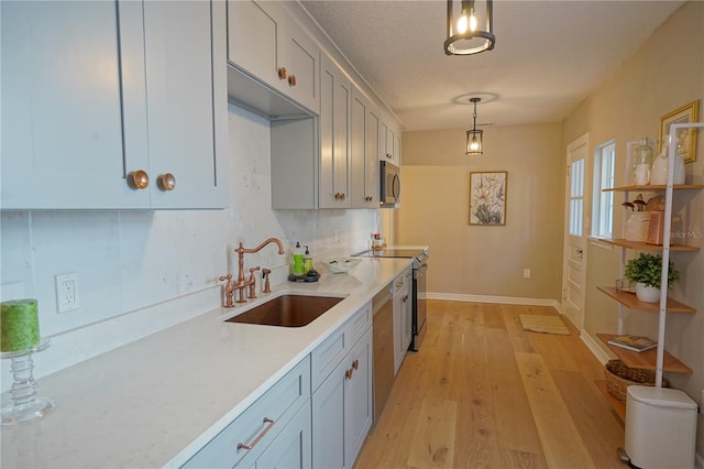 kitchen with appliances with stainless steel finishes, sink, hanging light fixtures, a textured ceiling, and light hardwood / wood-style flooring