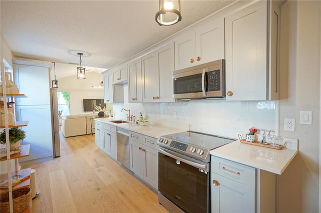 kitchen with appliances with stainless steel finishes, pendant lighting, sink, backsplash, and light wood-type flooring