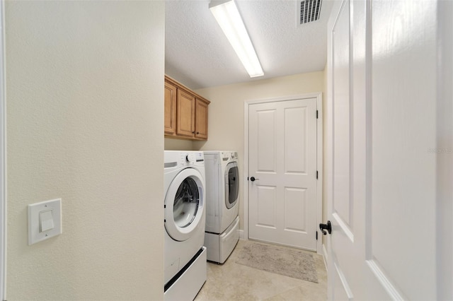 laundry area featuring cabinets, light tile patterned flooring, washer and dryer, and a textured ceiling