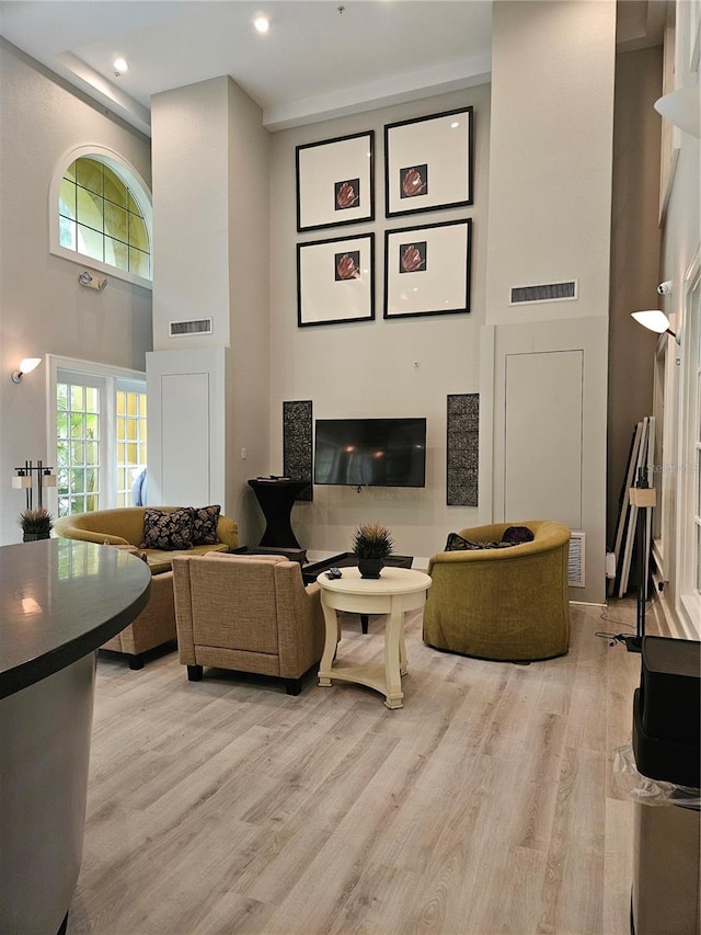 living room featuring a tile fireplace, light hardwood / wood-style flooring, and a towering ceiling