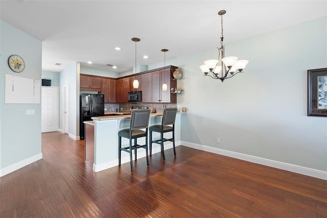 kitchen featuring black appliances, kitchen peninsula, pendant lighting, a breakfast bar area, and dark hardwood / wood-style floors