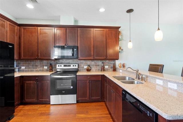 kitchen featuring black appliances, sink, hardwood / wood-style floors, decorative light fixtures, and a breakfast bar