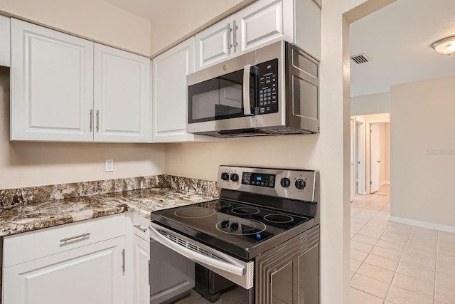 kitchen featuring dark stone countertops, white cabinetry, light tile patterned floors, and appliances with stainless steel finishes