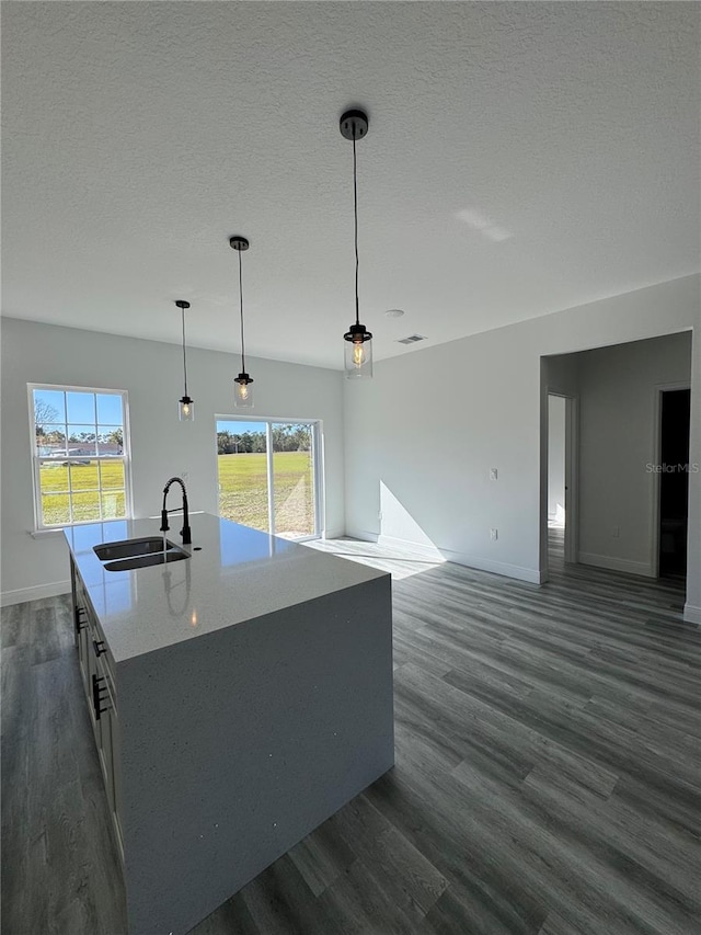 kitchen featuring dark wood-type flooring, sink, hanging light fixtures, a textured ceiling, and an island with sink