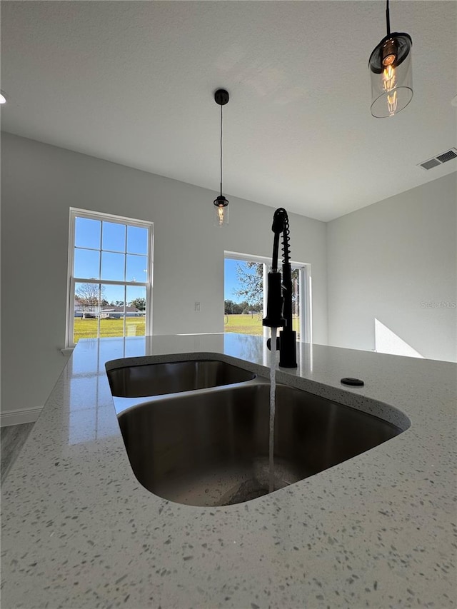 interior details with light stone counters, a water view, decorative light fixtures, and sink