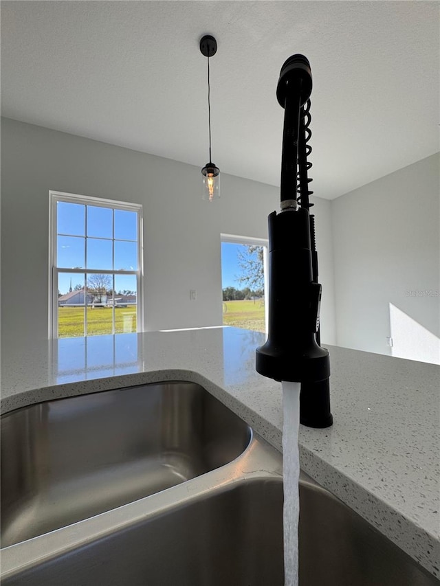 details featuring hanging light fixtures, light stone countertops, and sink