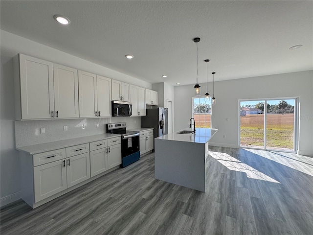 kitchen with appliances with stainless steel finishes, an island with sink, sink, white cabinets, and hanging light fixtures