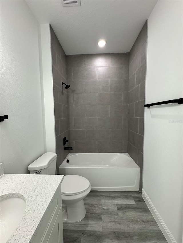 full bathroom featuring hardwood / wood-style flooring, tiled shower / bath, vanity, and toilet