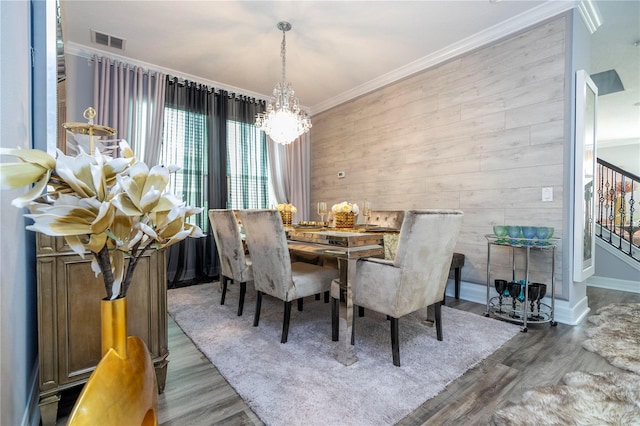 dining space featuring wood walls, wood-type flooring, ornamental molding, and an inviting chandelier