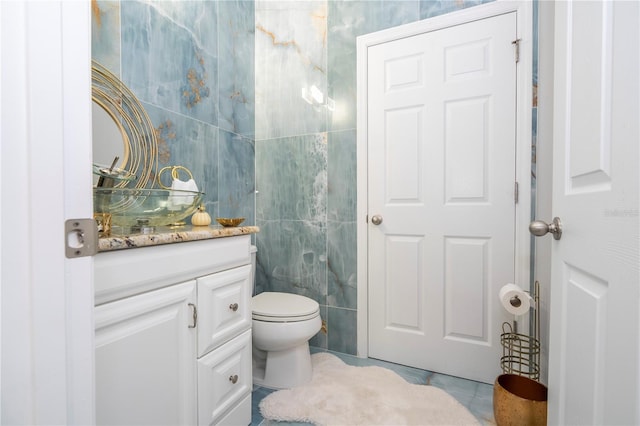 bathroom with tile walls, vanity, toilet, and tile patterned flooring