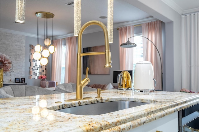 kitchen with crown molding, decorative light fixtures, sink, and light stone counters