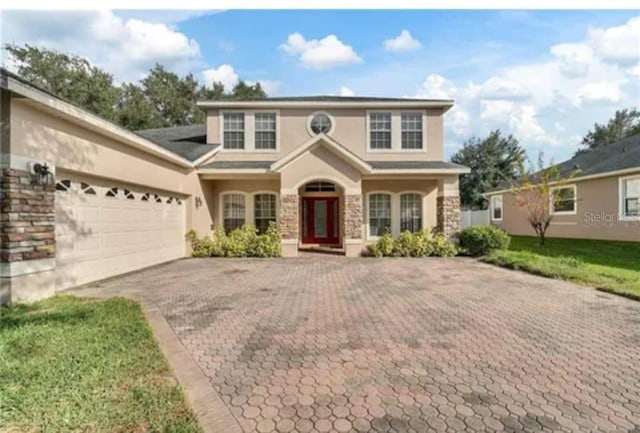 traditional-style home with a garage, stone siding, decorative driveway, and stucco siding