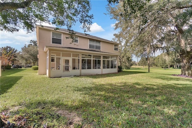 rear view of house featuring a sunroom, stucco siding, and a yard