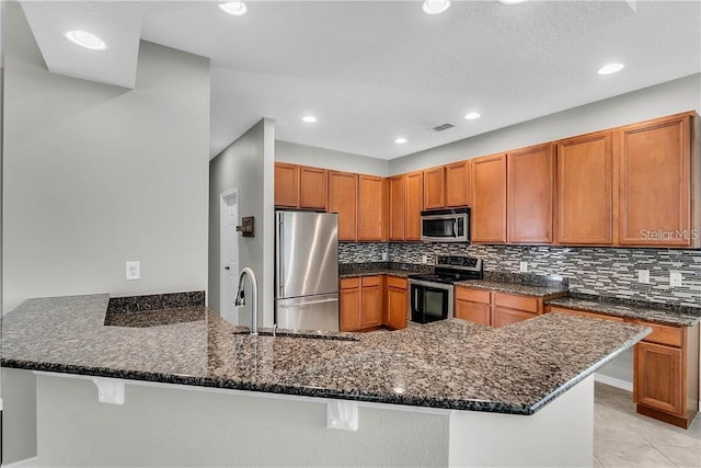 kitchen with stainless steel appliances, a peninsula, and dark stone countertops