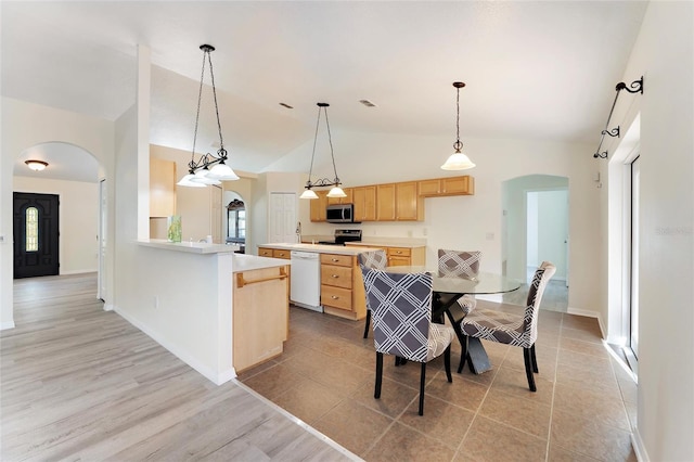 kitchen featuring light brown cabinets, light countertops, arched walkways, appliances with stainless steel finishes, and hanging light fixtures