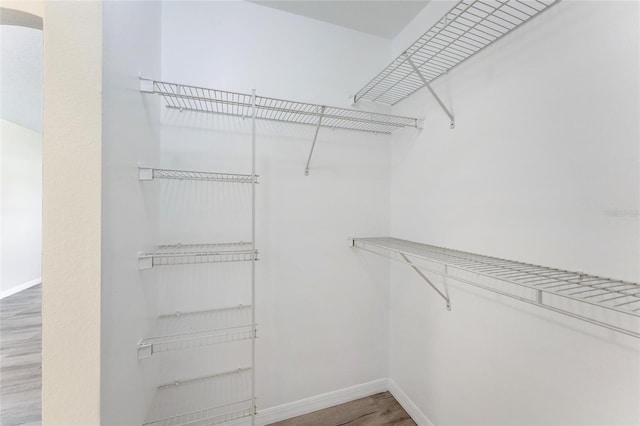 walk in closet with arched walkways and wood finished floors