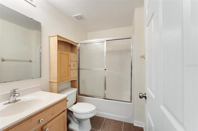 full bathroom featuring bath / shower combo with glass door, a textured ceiling, toilet, vanity, and tile patterned floors