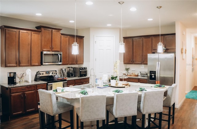 kitchen with a breakfast bar area, a kitchen island with sink, stainless steel appliances, sink, and decorative light fixtures