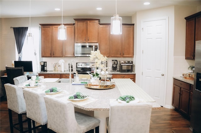 kitchen featuring a breakfast bar, appliances with stainless steel finishes, decorative light fixtures, and an island with sink